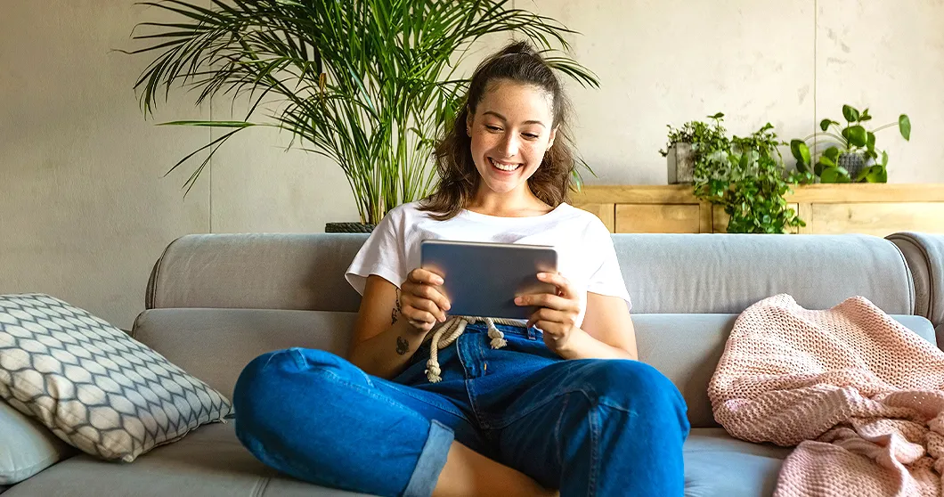 Lachende vrouw zit op de bank en houdt een tablet vast